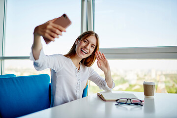 Funny female influencer in bluetooth earbuds waving while shooting video vlog via application on...