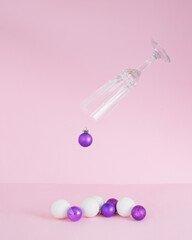 Christmas baubles coming out of champagne glass.Ornaments vivid violet and snowy white on a pink background.New Year holidays concept