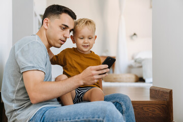 Young father and son using mobile phone while sitting on stairs