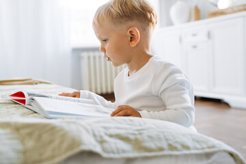 White blonde boy wearing home clothes reading book