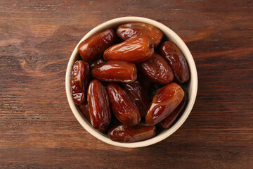 Sweet dried dates in bowl on wooden background, top view