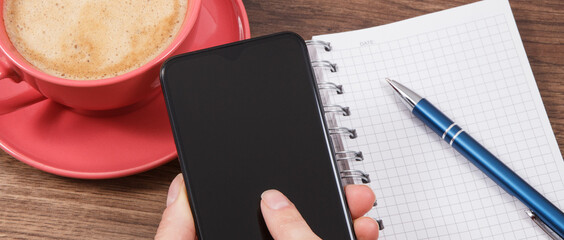Hand of woman with mobile phone, coffee with milk and notepad for notes. Work or relaxation