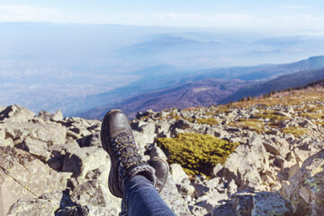Hiking  shoes on a mountain peaks background .Tourist woman sitting on the edge cliff mountains above the city 