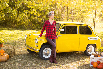 stylish hipster woman with short hair near yellow retro car in autumn park background with golden trees