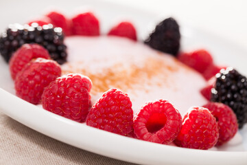 raspberries and blackberries laid out on a white plate in circle with yogurt and cinnamon