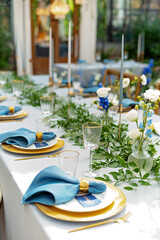 Banquet wedding table setting with blue napkins, gold cutlery, crystal, fresh flowers and candles. Wedding decorations. Soft selective focus.