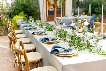 Fototapeta na wymiar Banquet wedding table setting with blue napkins, gold cutlery, crystal, fresh flowers and candles. Wedding decorations. Soft selective focus.