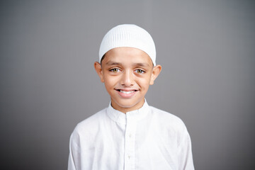 smiling Muslim child with traditional cap by looking at camera on gray background - concept showing of Happiness, positive emotion during childhood