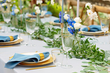 Banquet wedding table setting with blue napkins, gold cutlery, crystal, fresh flowers and candles. Wedding decorations. Soft selective focus.