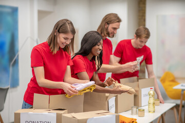 Young peeple in red packing the cardboards with humanitarian help