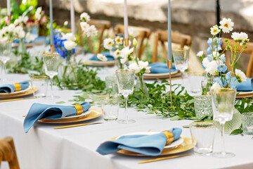 Banquet wedding table setting with blue napkins, gold cutlery, crystal, fresh flowers and candles....