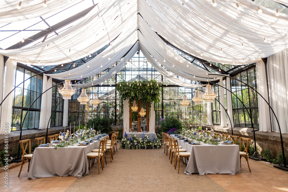 Wall mural wedding banquet hall in the greenhouse, tables are set, decorated with fresh flowers, candles, cryst