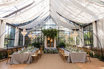 Wedding banquet hall in the greenhouse, tables are set, decorated with fresh flowers, candles,...