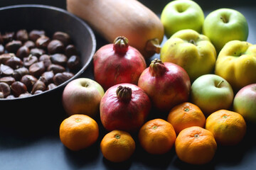 Pan with chestnuts, butternut squash and various fruit on dark background. Selective focus.