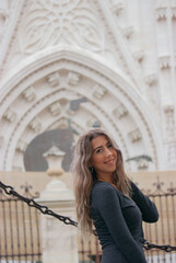 Caucasian tourist girl poses smiling towards the camera with Seville cathedral in the background.