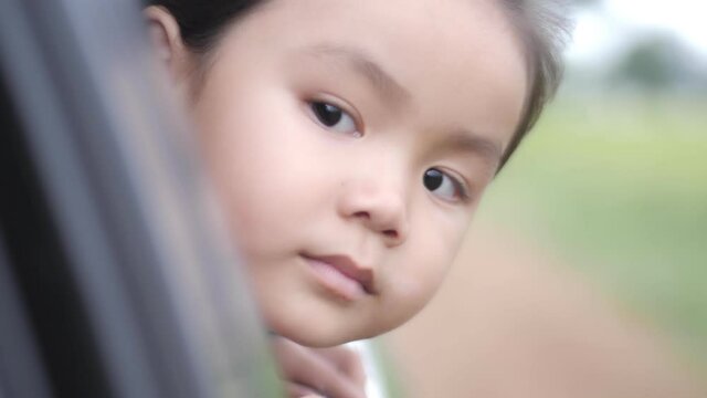 Slow motion scene ofA 4-5 year old Asian girl is sitting in a car looking out of the side mirror.