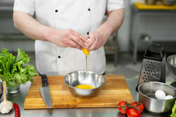 Cook breaks an egg. Egg yolk falling into the bowl