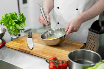 Chef whips eggs with his hands in a bowl to make an omelet with vegetables