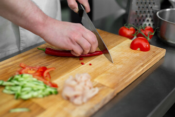 Chef man cutting chili peppers at table, closeup
