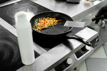 Close-up of the hands of a chef who is frying meat and vegetables in a pan in a restaurant