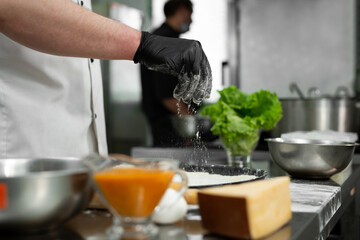 Preparation of the dough for pizza. Close-up of the cook's hand sprinkling the dough with flour