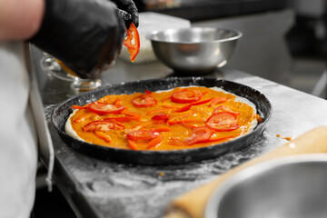 Cooking pizza. Close-up of the chef's hand spreading slices of tomato on the dough