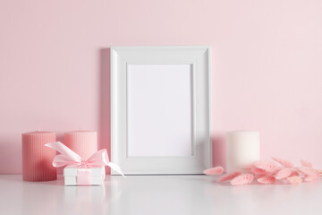 Empty photo frame mockup, candles, dry pink flowers on a white table, against background of pink wall.