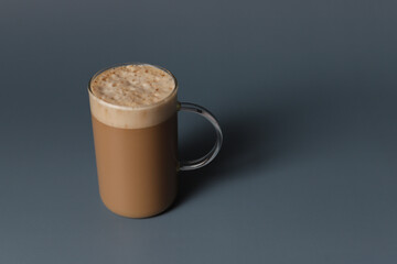 Glass cup of hot caramel cappuccino with bubbles on grey background.