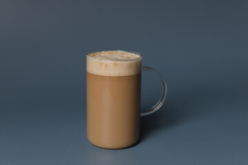 Glass cup of hot caramel cappuccino with bubbles on grey background.