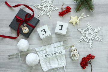 Calendar for December 31: New Year's decor, a gift tied with a red ribbon, knitting from white yarn, spruce branches and viburnum berries, number 31, the name of the month in English.
