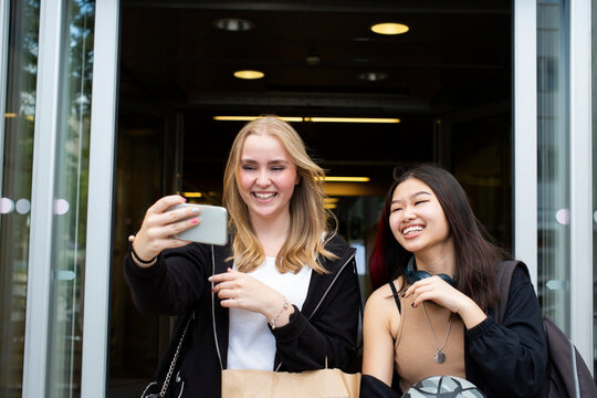 Smiling female friends taking selfie on smart phone at shopping mall
