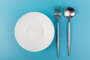 Empty plate with fork and spoon on blue background. Flat lay Dishes for breakfast, lunch or dinner Mock up