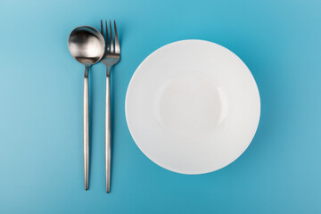 Empty plate with fork and spoon on blue background. Flat lay Dishes for breakfast, lunch or dinner Mock up