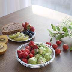 Fresh raw organic berries and exotic fruits in round glass plate on wooden table. cabbage,,kiwi, strawberry.