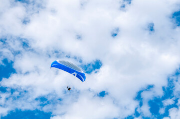 Obraz premium Paraglider flying into the sky with clouds on a sunny day.