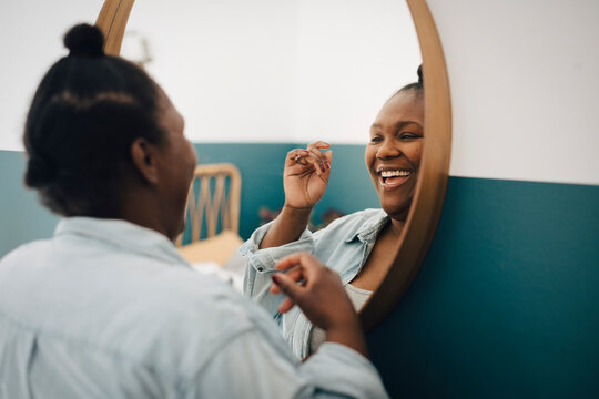 Happy mid adult woman looking in mirror at home - Powered by Adobe