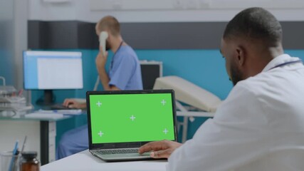 African american doctor looking at mock up green screen chroma key laptop computer with isolated display. Therapist man analyzing sickness diagnostic working at medical report in hospital office