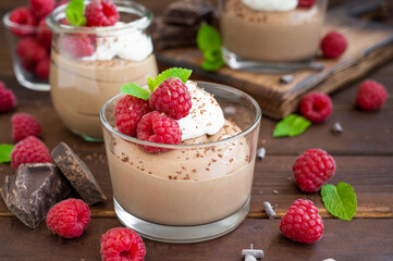 Chocolate mousse with whipped cream and fresh raspberries in a glass on a dark wooden background. Copy space.