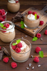Chocolate mousse with whipped cream and fresh raspberries in a glass on a dark wooden background. Copy space.