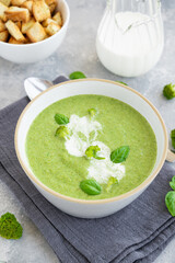 Broccoli cream soup with fresh basil and croutons in a bowl on a gray concrete background. Copy space.