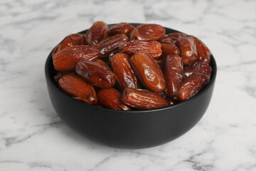 Sweet dried dates in bowl on white marble table