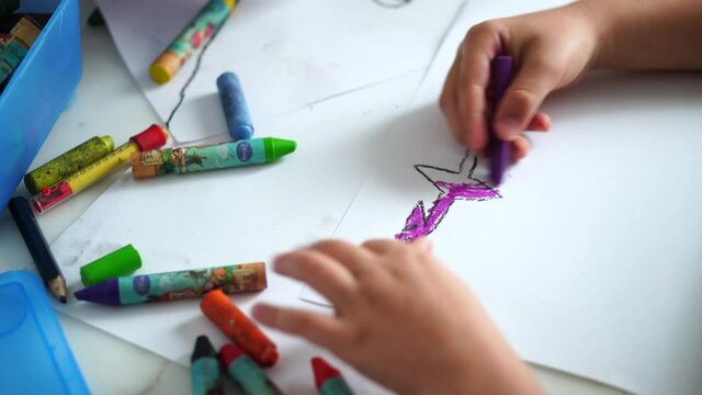 POZNAN, POLAND - Nov 07, 2021: A young child drawing and coloring dinosaurs on white paper by a table.