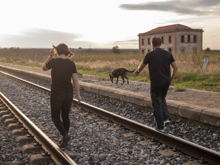 Adult couple walking with their dog on a railroad during sunset