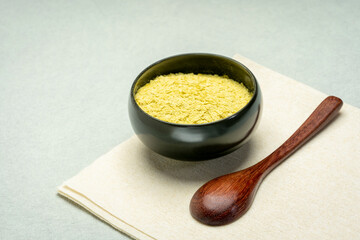nutritional organic yeast flakes in a small ceramic bowl with a wooden teaspoon, nutrition...