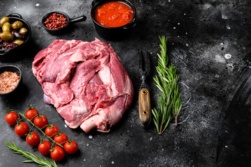 Raw lamb shoulder meat ready for baking, with ingredients and herbs, on black dark stone table background, with copy space for text