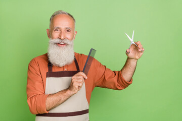 Portrait of attractive cheerful skilled well-groomed grey-haired man holding equipment isolated over green color background