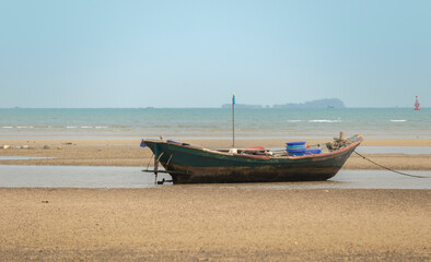 fisherman's fishing boat on sand at a fishing village beach There is an island and sea background with the daytime sky.  stranded fishing boat After the sea has receded
