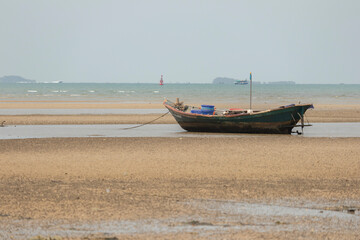 fisherman's fishing boat on sand at a fishing village beach There is an island and sea background with the daytime sky.  stranded fishing boat After the sea has receded
