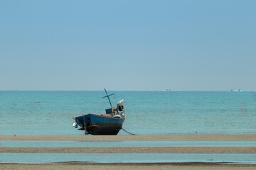 Fototapeta premium fisherman's fishing boat on sand at a fishing village beach There is an island and sea background with the daytime sky. stranded fishing boat After the sea has receded