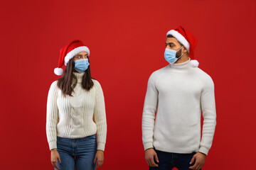 Social distancing during covid-19 lockdown. Arab spouses in Santa hats and protective masks looking at each other